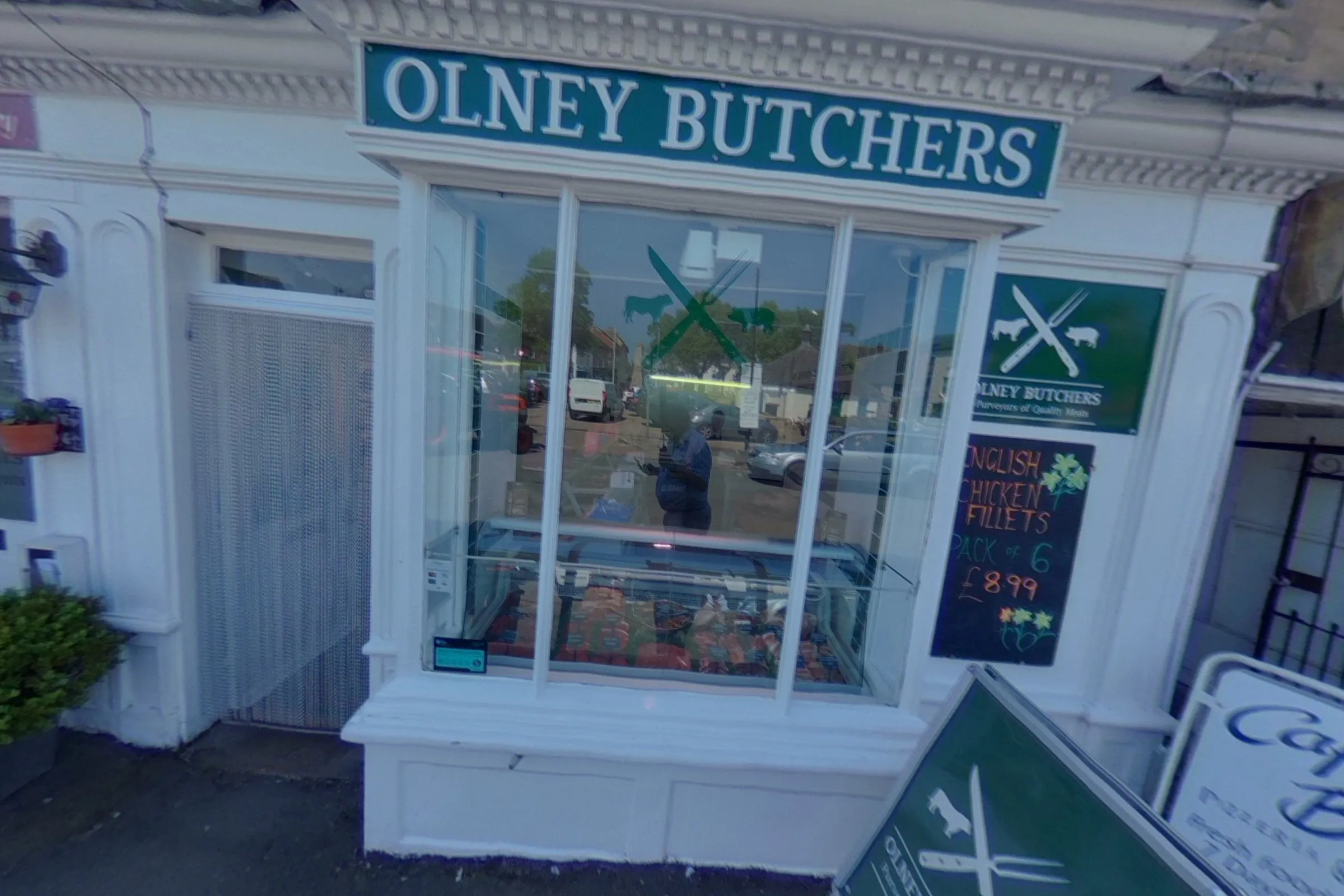 The Olney Butchers shopfront: white painted Georgian woodwork, the green fascia lettered OLNEY BUTCHERS, the counter seen through the window and a green A-board on the pavement